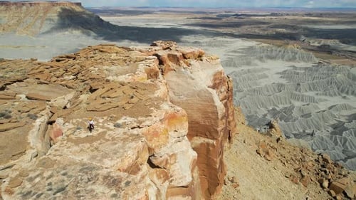Aerial View of Lonely Woman Walking on Top of Mesa Near Cliff Edge Above Badlands of Utah USA