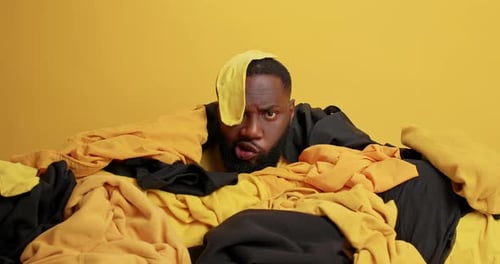 Dark Skinned Man Collects Laundry for Washing Poses Near Pile of Clothes
