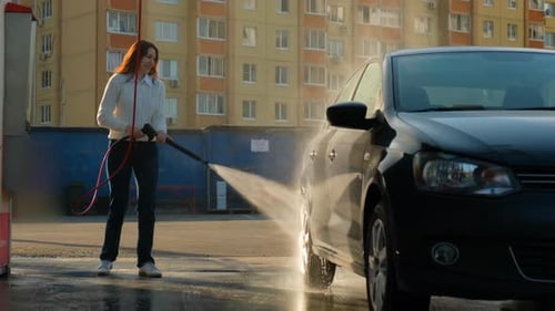 A Woman Rinses a Car with Water at a Car Wash with Strong Pressure