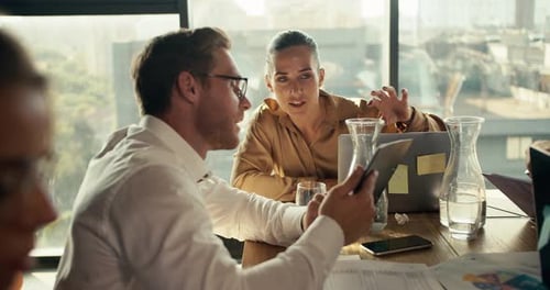An Office Worker in a Shirt and Glasses Shows His Project on a Tablet to a Blonde Woman Sitting at a