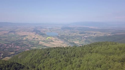 Aerial view from drone of paragliding. Person in far distance, under large yellow parachute fly high