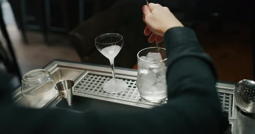 A professional bartender is mixing an alcoholic cocktail with ice cubes to customers at the bar or