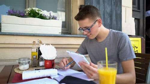 Young handsome student doing homework with tablet computer in a cafe