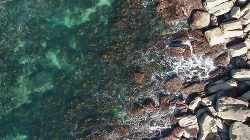 Top down birds eye view drone shot of waves crashing into jagged rocks off the coastline of Australi