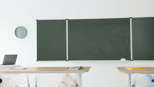 Green chalkboard, backpacks and stylish furniture in classroom. Camera moving left