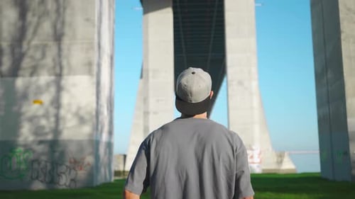 Man Standing with Skateboard Under Bridge