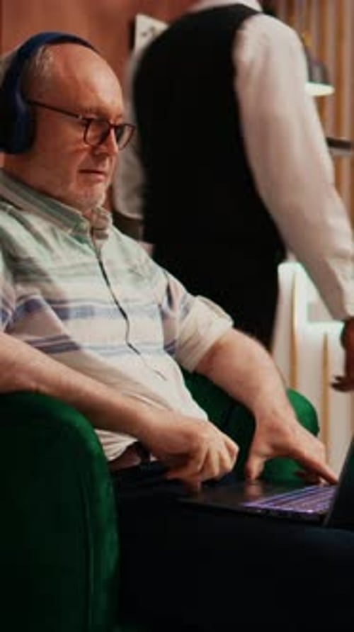 Senior man with headphones using laptop in armchair