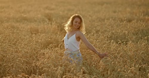 Beautiful Woman is Spinning in a Wheat Field Holding a Hat in Her Hands