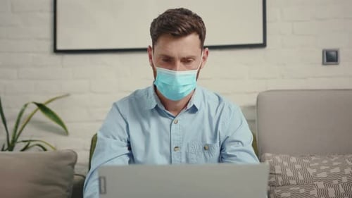 Close Up Man Wearing Medical Protective Mask While Working on Wireless Laptop at Home Self Isolation