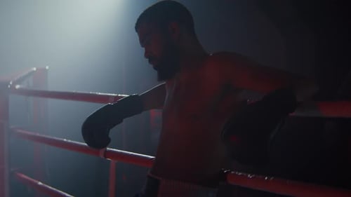 Der müde afroamerikanische Boxer lehnt sich an Seile, die auf dem Ring ruhen