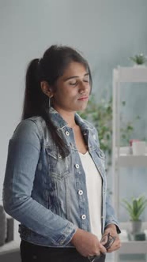 Une femme indienne pensive en veste en jean regarde par la fenêtre lumineuse