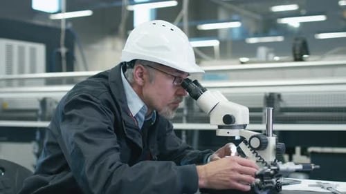 Un ingénieur principal inspecte un détail au microscope dans une usine.