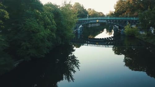 Drone aerial river in a park during sunrise with a bridge reflecting on the water