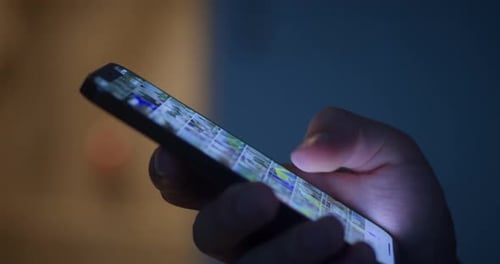 Hand Holding and Scrolling Mobile Phone at Night