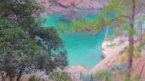 A top view of an island over the trees with crystal clear green water, surrounded with mountains.