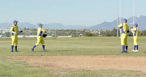 Raising glove, diverse male teammates practicing catch-and-throw drill in outfield, with baseballs