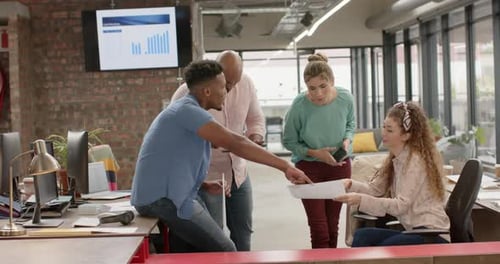 Diverse creative business colleagues discussing document in casual office, in slow motion