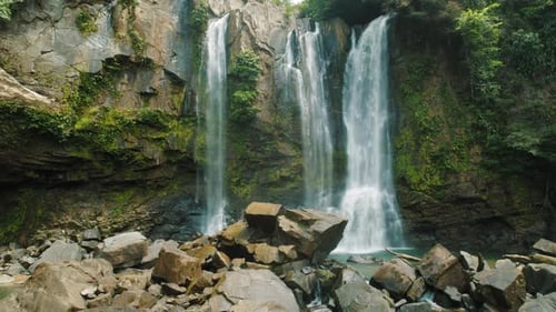 Close view of tall tropical waterfalls cascading over rocky cliffs into pool