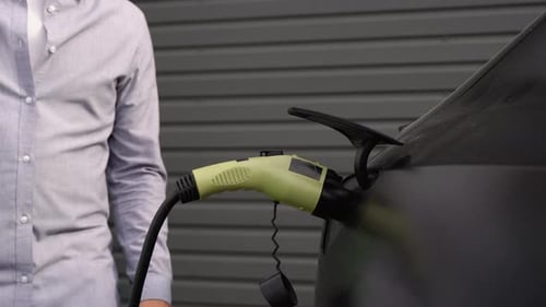A Man Disconnects a Charging Cable to an Electric Car Close Up