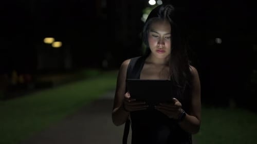 Beautiful young woman using digital tablet computer outdoors at night