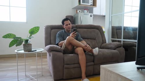 Man Relaxing on Sofa Using Smartphone at Home