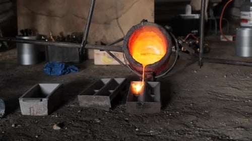Slow motion bucket full of molten metal poured into moulds in a rustic foundry