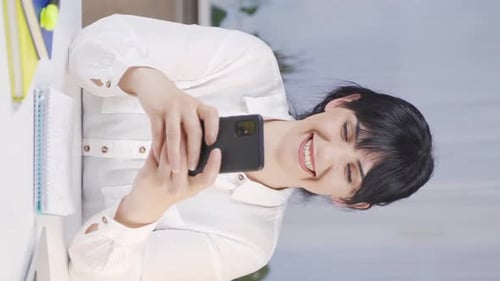 Woman Using Phone and Writing in Notebook at Desk