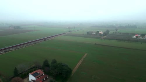 High DRONE shot of a HIGH-SPEED TRAIN crossing farmland on a foggy winter day