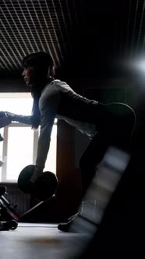 Woman Doing Dumbbell Rows in Dark Gym