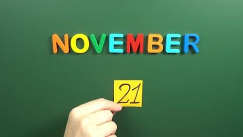 Hand sticking a sticker 21 November calendar day on school board. 21 date of November. Twenty first