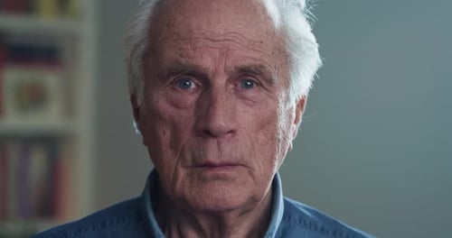 Cinematic shot of happy senior pensioner man is smiling in camera in living room at home. Concept