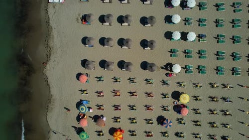 Colorful beach umbrellas and sunbeds lined up on sandy beach, lapped by salty waters of shallow lago