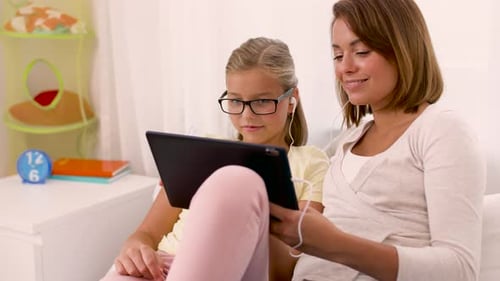 Woman and girl with tablet wearing headphones at home