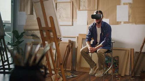 Male Artist Using VR Headset to Paint in His Bright Studio Surrounded By Artwork