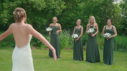 Bride shows off her dress as bridesmaids turn around with excitement and joy in a garden