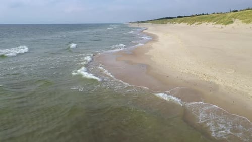 AERIAL: Flying Backwards Over Beach with Waves Crashing on the Shore during Golden Hour Evening