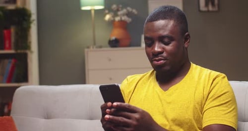 Young Man Using Mobile Phone Sitting on Sofa