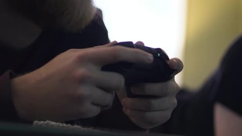 Close up shot on the hands holding a video game controller, with another man's feet kicking around i
