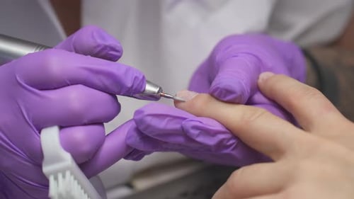 Nageltechniker verwendet eine elektrische Feile, um die Nägel eines Kunden während einer Maniküre zu formen und vorzubereiten