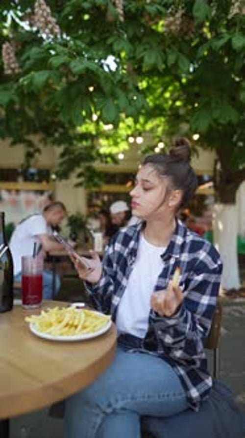 Engaging in a Delicious Snack a Stunning Girl is Eating French Fries on a Summer Café Terrace