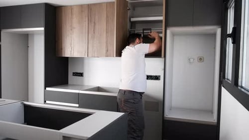 Young latin man installing an accessible kitchen cabinet in the kitchen.