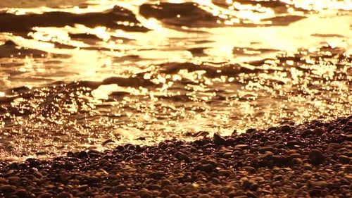 Meer, Strand, Welle, Meereswellen mit weichem, schaumigem Wasser, das mehrfarbige Kieselsteine am Strand wäscht