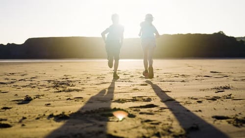 Children Running On Sandy Beach In Setting Sun