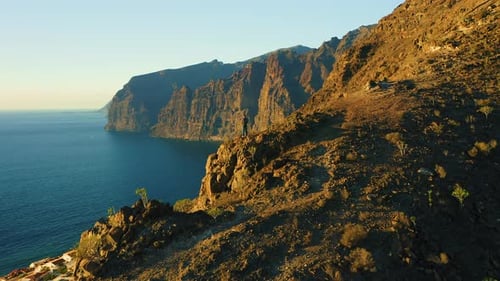 Man Stands on Edge of Sheer Cliff with Ocean View