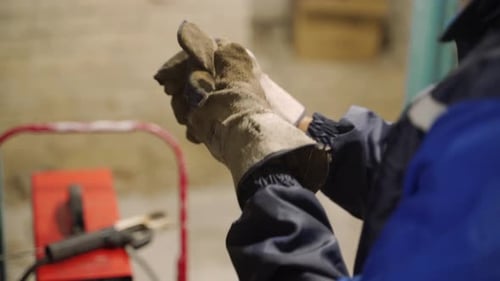 Close Up Shot of Professional Welder's Hands While Putting on Protective Gloves in Front of Welding