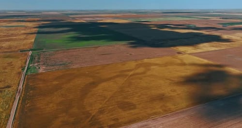 Huge field looking like a patchwork quilt. A shadow of a big cloud is on the ground. Top view.