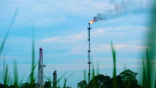 Fire burning on top of gas flare stack chimney on petroleum refinery with crops in the foreground