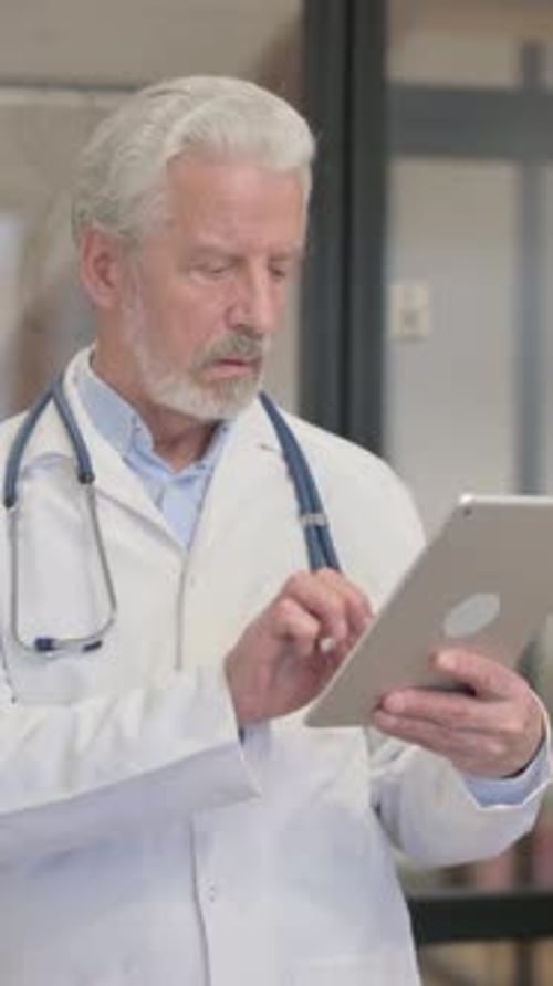 Senior Old Doctor Using Digital Tablet while Standing in Hospital, vertical video