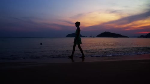 Woman Walks Silhouetted on Tropical Beach at Sunset