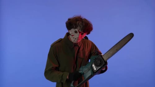 Man in White Mask with Chainsaw in Hands on Blue Background with Red Neon Light Image of Jason